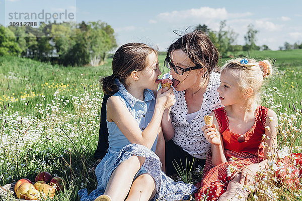 Mutter und zwei Mädchen auf der Wiese essen Eistüten