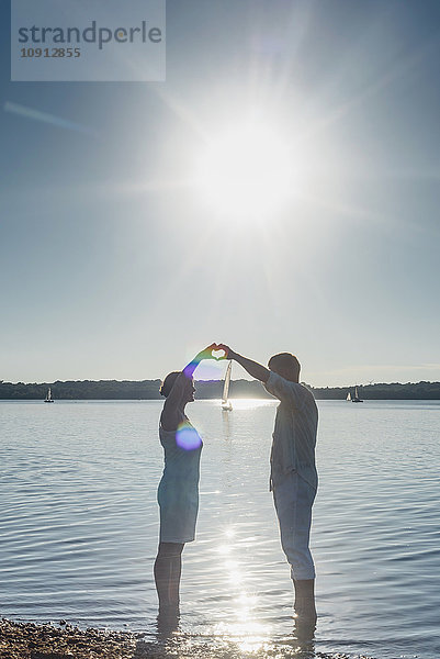 Paar steht am Cospudener See und bildet mit den Händen ein Herz gegen die Sonne.