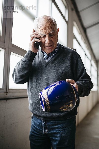 Älterer Mann beim Durchsehen der Keramikvase  beim Telefonieren