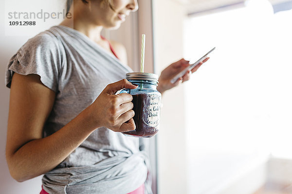 Junge Frau mit gesundem Getränk beim Blick aufs Handy