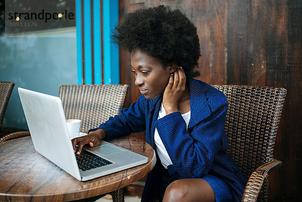 Junge Frau arbeitet mit Laptop in einem Straßencafé