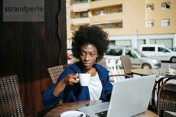 Junge Frau mit Laptop in einem Straßencafé beim Kaffeetrinken
