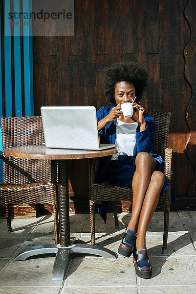 Junge Frau mit Laptop in einem Straßencafé beim Kaffeetrinken