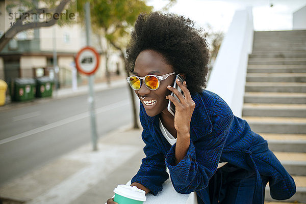 Porträt einer jungen Frau mit verspiegelter Sonnenbrille im Gespräch auf dem Handy
