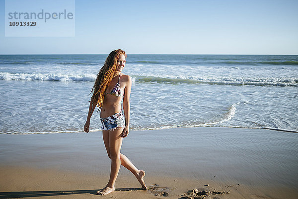 Lächelnde junge Frau beim Spaziergang am Strand