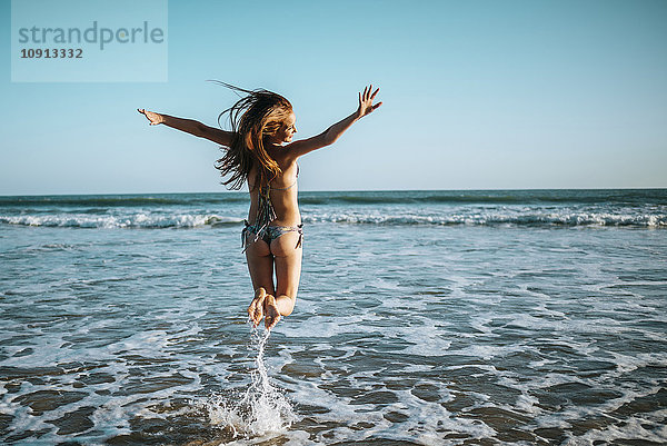 Begeisterte junge Frau beim Springen am Strand