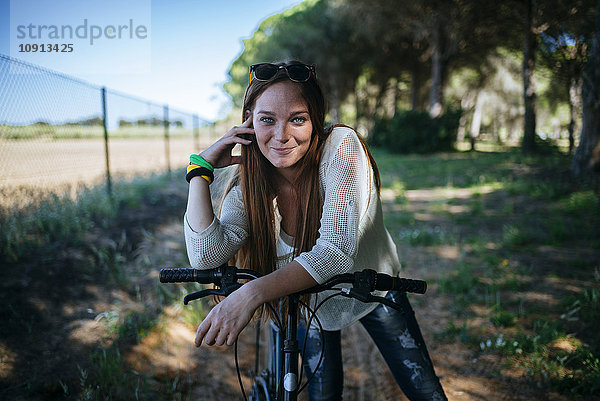 Lächelnde junge Frau mit Fahrrad in ländlicher Landschaft