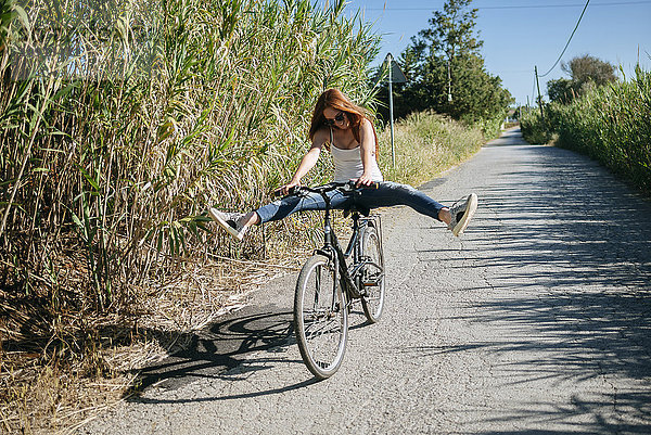 Verspielte junge Frau beim Radfahren auf dem Landweg