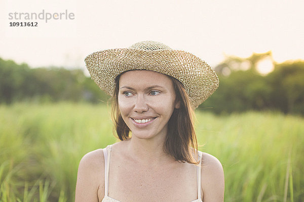 Porträt einer lächelnden Frau mit Sommerhut in der Natur