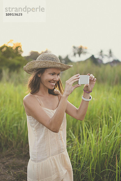 Lächelnde Frau beim Fotografieren mit dem Smartphone in der Natur