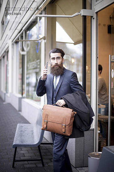 Hipster mit Aktentasche und Smartphone beim Verlassen des Cafés