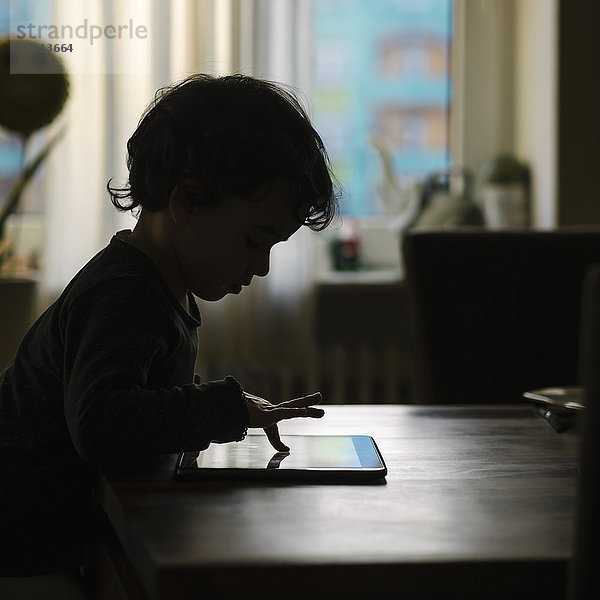 Silhouette eines kleinen Mädchens  das zu Hause mit einem digitalen Tablett spielt.