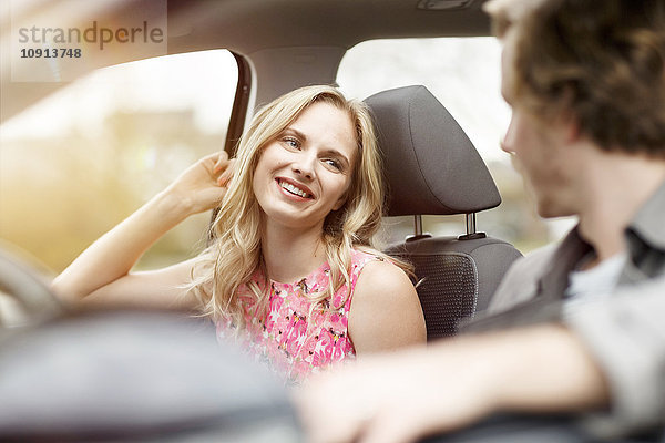 Porträt einer lächelnden blonden Frau  die auf einem Beifahrersitz im Auto sitzt und mit ihrer Freundin spricht.