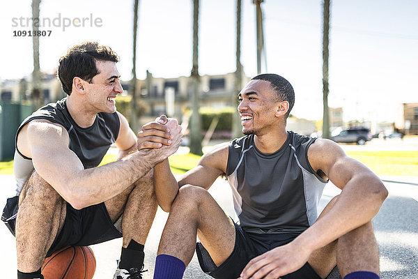 Zwei junge Männer beim Händeschütteln auf dem Basketballplatz im Freien