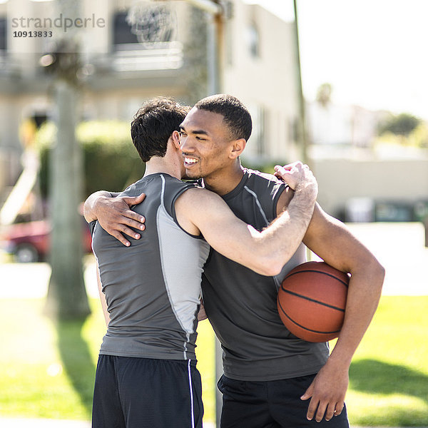 Zwei Basketballspieler  die sich im Freien umarmen.