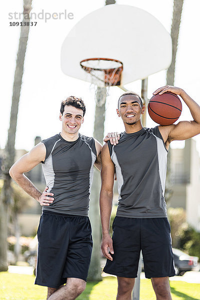 Porträt von zwei lächelnden jungen Männern auf dem Basketballplatz im Freien