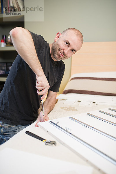 Mann beim Zusammenbau von Möbeln zu Hause mit Schraubendreher