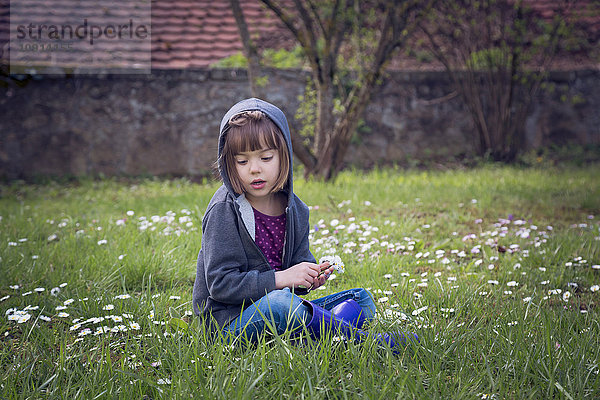 Mädchen in Kapuzenjacke auf Blumenwiese sitzend