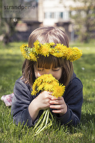 Kleines Mädchen mit Blumenkranz auf Wiese liegend duftende Löwenzähne