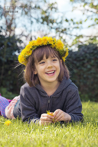 Porträt eines lächelnden kleinen Mädchens auf der Wiese mit Blumenkranz aus Löwenzahn