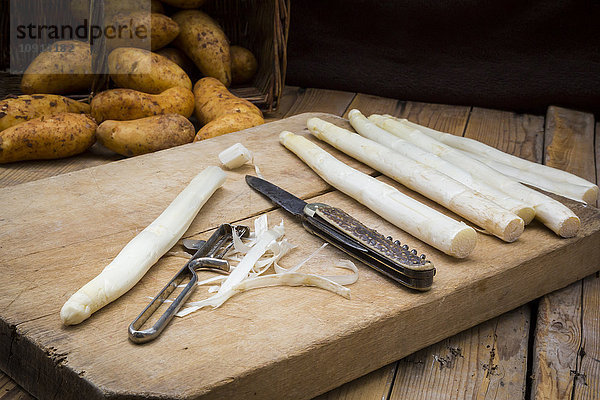 Weißer Spargel  Taschenmesser und Schäler auf Holzplatte