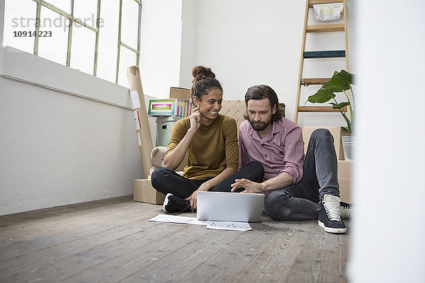 Paar sitzt auf dem Boden der neuen Wohnung mit Laptop