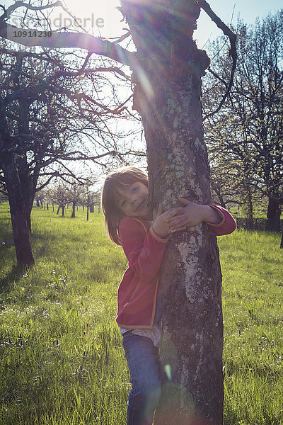 Porträt eines lächelnden kleinen Mädchens  das den Baum umarmt.