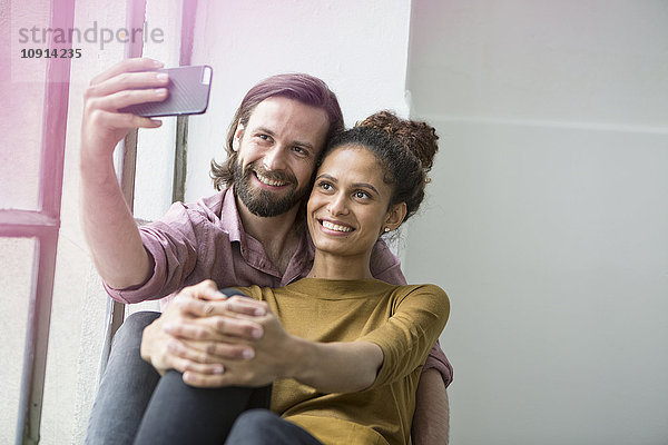 Junges Paar sitzt auf der Fensterbank und nimmt Selfie mit Smartphone