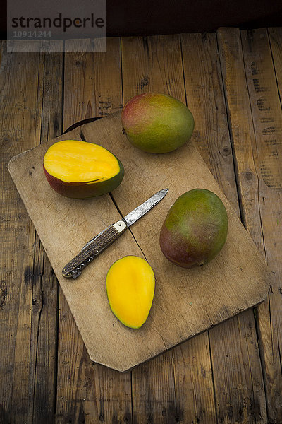 Ganze und geschnittene Mango und Taschenmesser auf Holzplatte