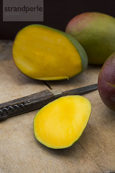 Ganze und geschnittene Mango und Taschenmesser auf Holz
