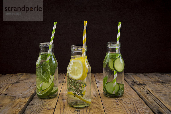 Drei Glasflaschen Tafelwasser mit unterschiedlichen Früchten und Kräutern