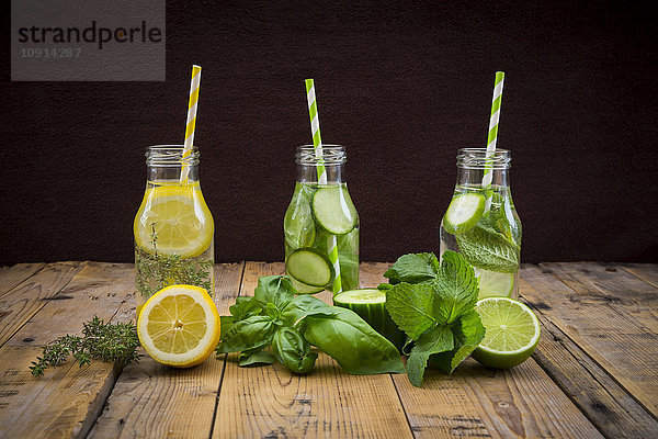 Drei Glasflaschen Tafelwasser mit unterschiedlichen Früchten und Kräutern
