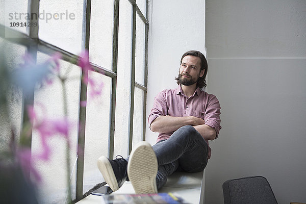 Mann sitzt auf der Fensterbank und schaut aus dem Fenster.