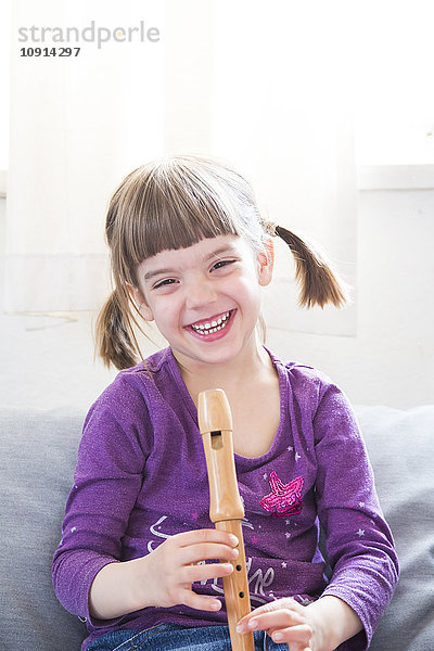 Lachendes kleines Mädchen mit Blockflöte zu Hause