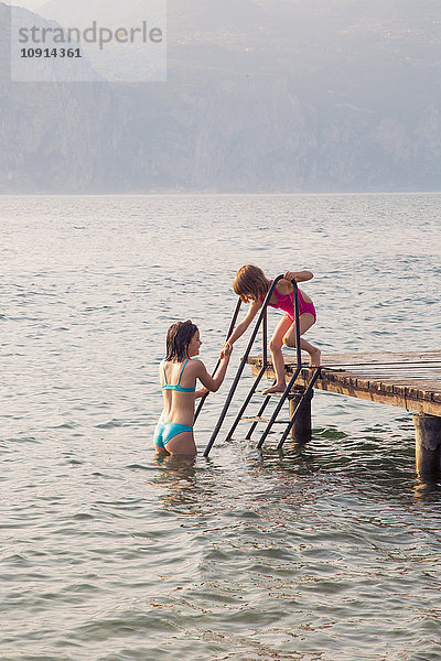 Italien  Brenzone  Mädchen hilft ihrer kleinen Schwester vom Steg in den See