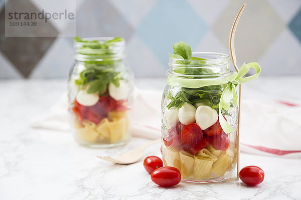 Calabrese-Salat mit Nudeln  Tomaten  Mozzarella  Rucola und Basilikum in Gläsern