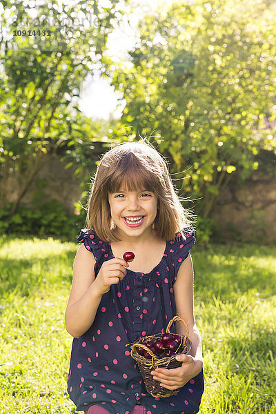 Porträt eines lachenden kleinen Mädchens  das im Garten Kirschen isst.