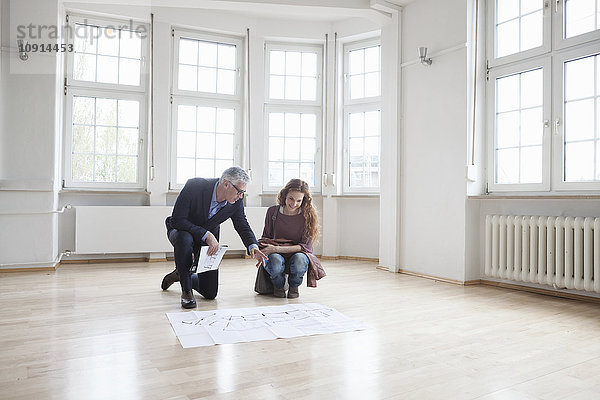 Immobilienmakler zeigt dem Kunden den Bauplan in einer leeren Wohnung.