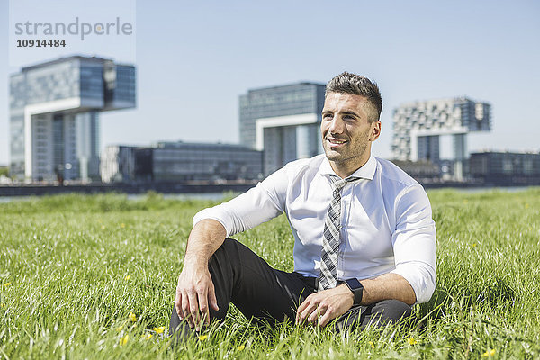 Deutschland  Köln  lächelnder Geschäftsmann auf der Wiese sitzend