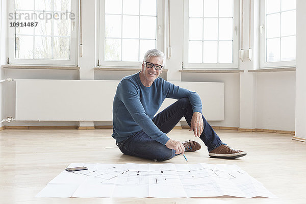 Porträt eines lächelnden Mannes mit Bauplan in leerer Wohnung