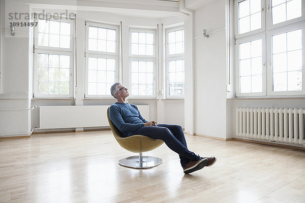 Mann sitzend im Sessel in leerer Wohnung