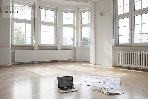 Laptop und Bauplan auf Etage in leerer Wohnung