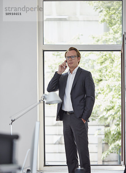 Geschäftsmann im Büro vor offenem Fenster telefonieren mit Smartphone