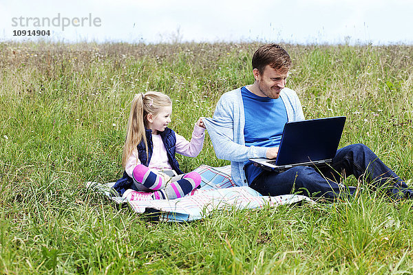 Vater und Tochter sitzen auf der Wiese  Smartphone und Laptop