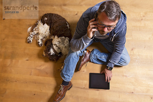 Overhead-Ansicht des Mannes am Telefon auf dem Boden neben dem Hund
