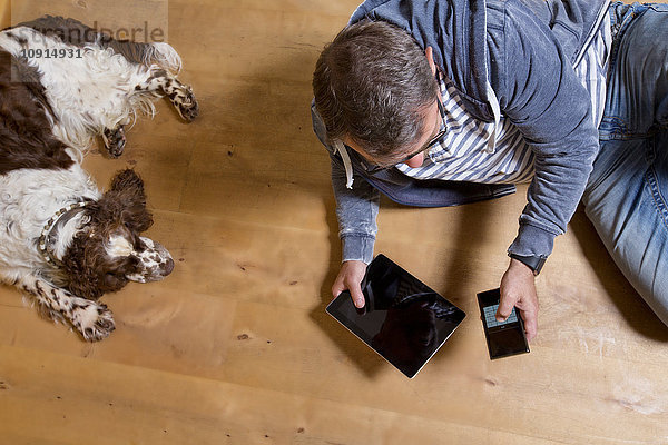 Overhead-Ansicht des Mannes mit Smartphone auf dem Boden neben dem Hund