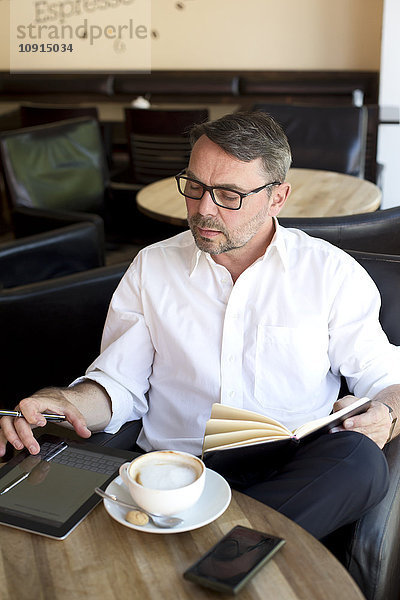 Geschäftsmann  der in einem Café sitzt und ein digitales Tablett benutzt