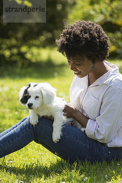 Junge Frau auf einer Wiese sitzend mit ihrem Hund auf dem Schoß