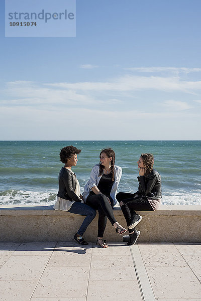Drei junge Frauen  die am Meer sitzen und reden.