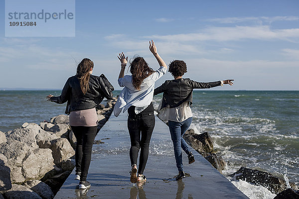 Drei junge Frauen haben Spaß auf dem Wellenbrecher am Meer